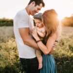 Un couple se tient dans un champ ensoleillé, souriant affectueusement au bébé qu'ils tiennent entre eux. Cette scène chaleureuse reflète magnifiquement la communication positive parentale, l'amour et la connexion brillant entre les parents et leur bébé heureux.