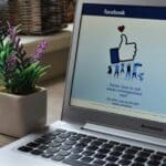 Un ordinateur portable affichant la page d'inscription Facebook est posé sur un bureau en bois à côté d'une petite plante en pot au feuillage violet et vert - une configuration invitante pour quiconque cherche à animer une communauté.